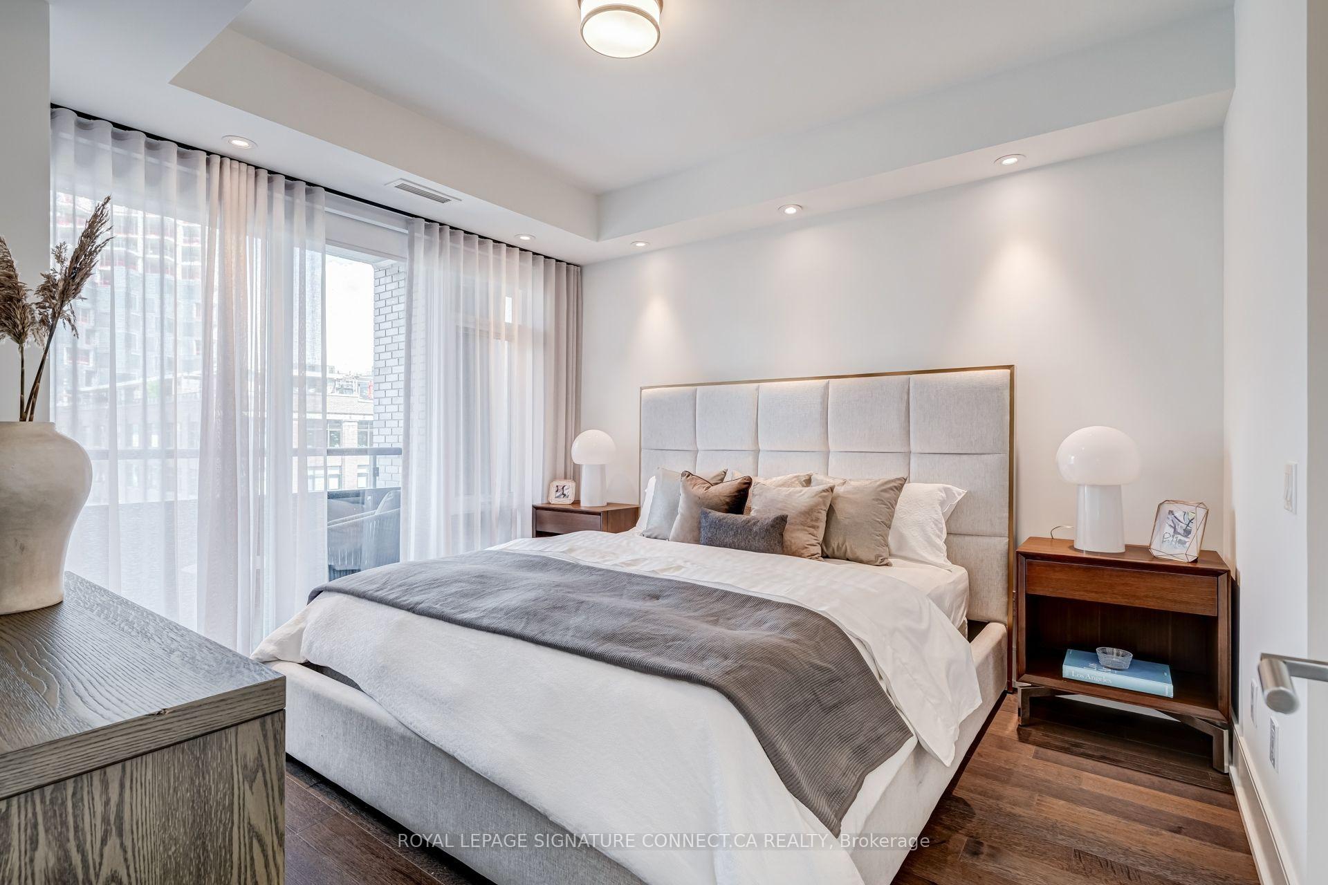 Staged bedroom with an upholstered bed, wood nightstands, and floor-to-ceiling sheer curtains.