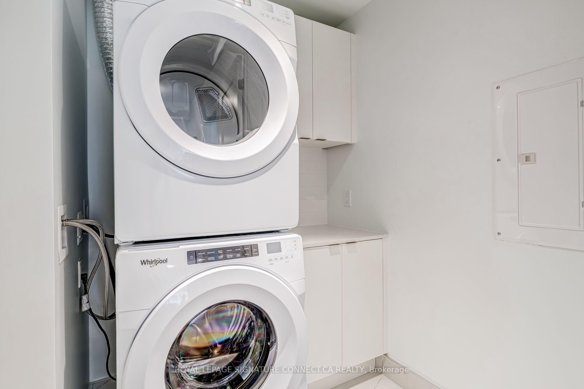 Laundry room with stacked white front-loading washer and dryer beside built-in cabinets and counter.