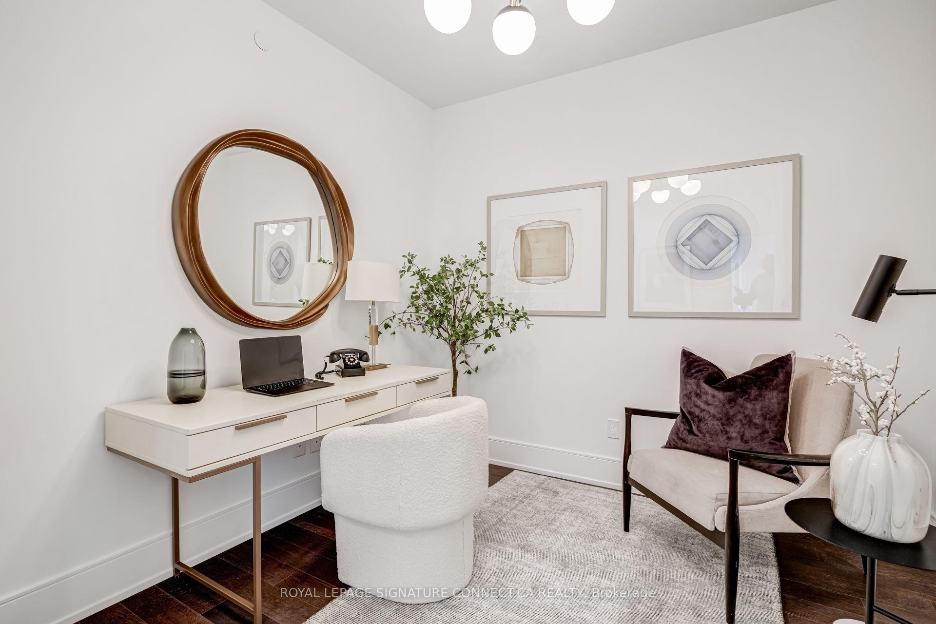 Furnished home office with a white desk, round wood-framed mirror, and cream lounge chair.