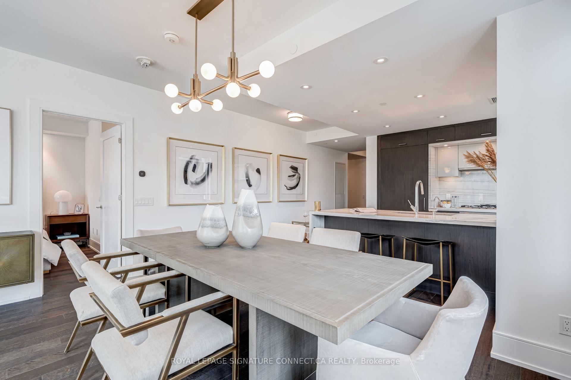 Dining area with a large pale table, upholstered chairs, and an open kitchen with dark cabinetry.