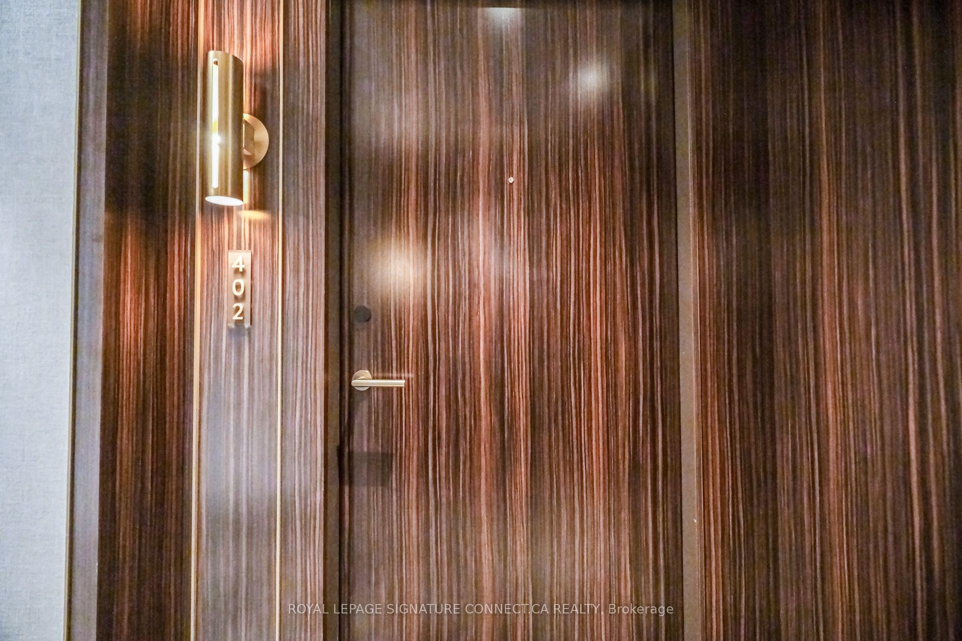 Wood-grain entry door marked 402, with a brass-colored handle and illuminated wall sconce.