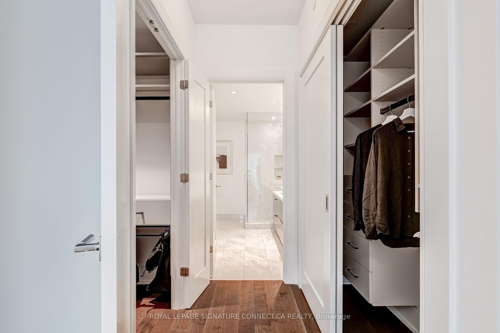 Dressing hallway with built-in closets leading to a marble-tiled bathroom and glass shower.