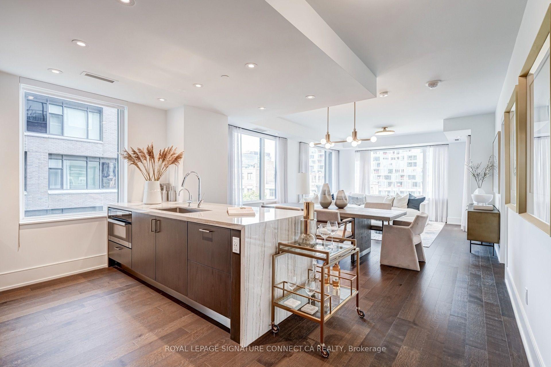 Open-plan condo kitchen with a marble island, dining area, and bright living room beside large windows.