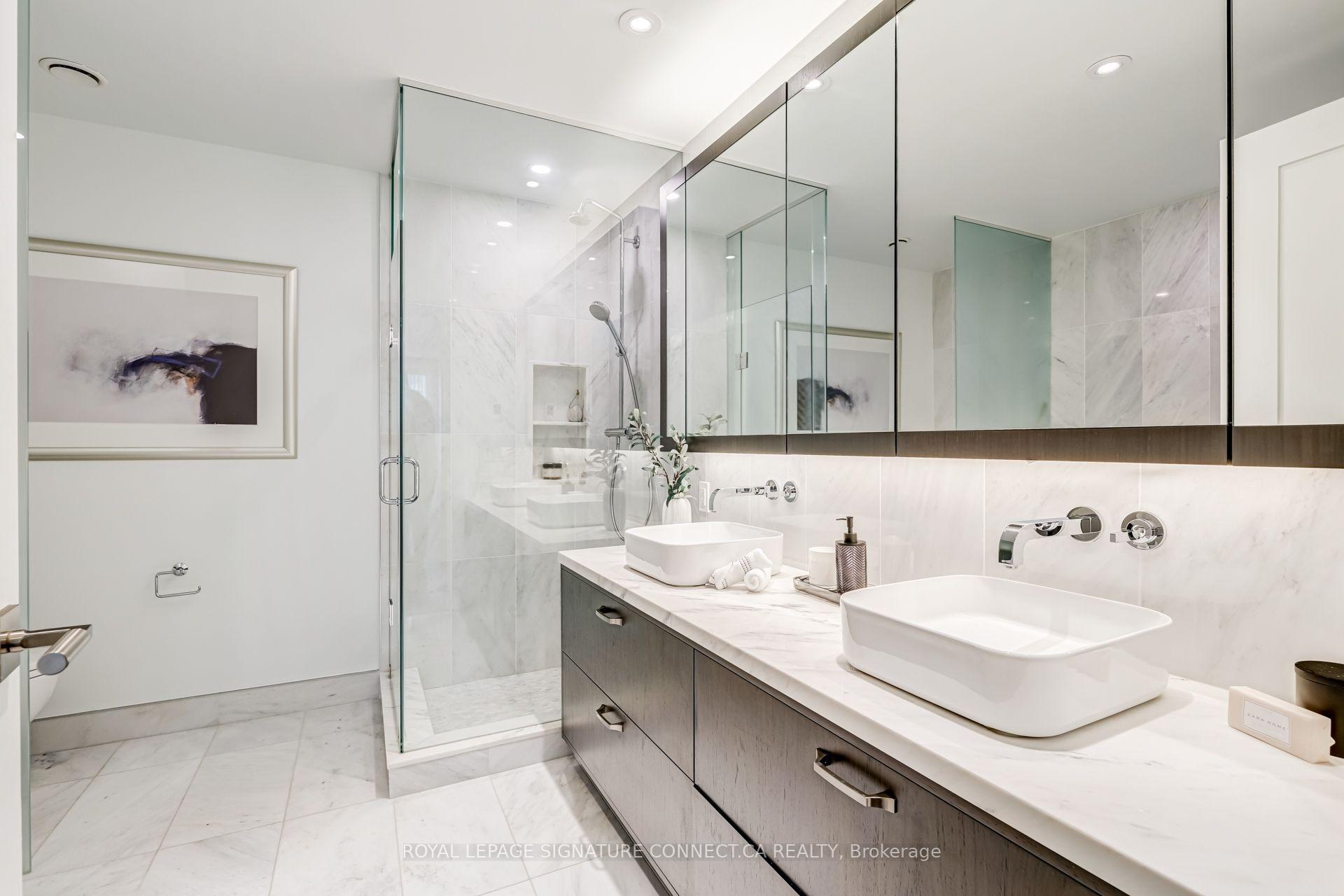 Marble bathroom with double vessel sinks, a glass shower, and a long dark-wood vanity.