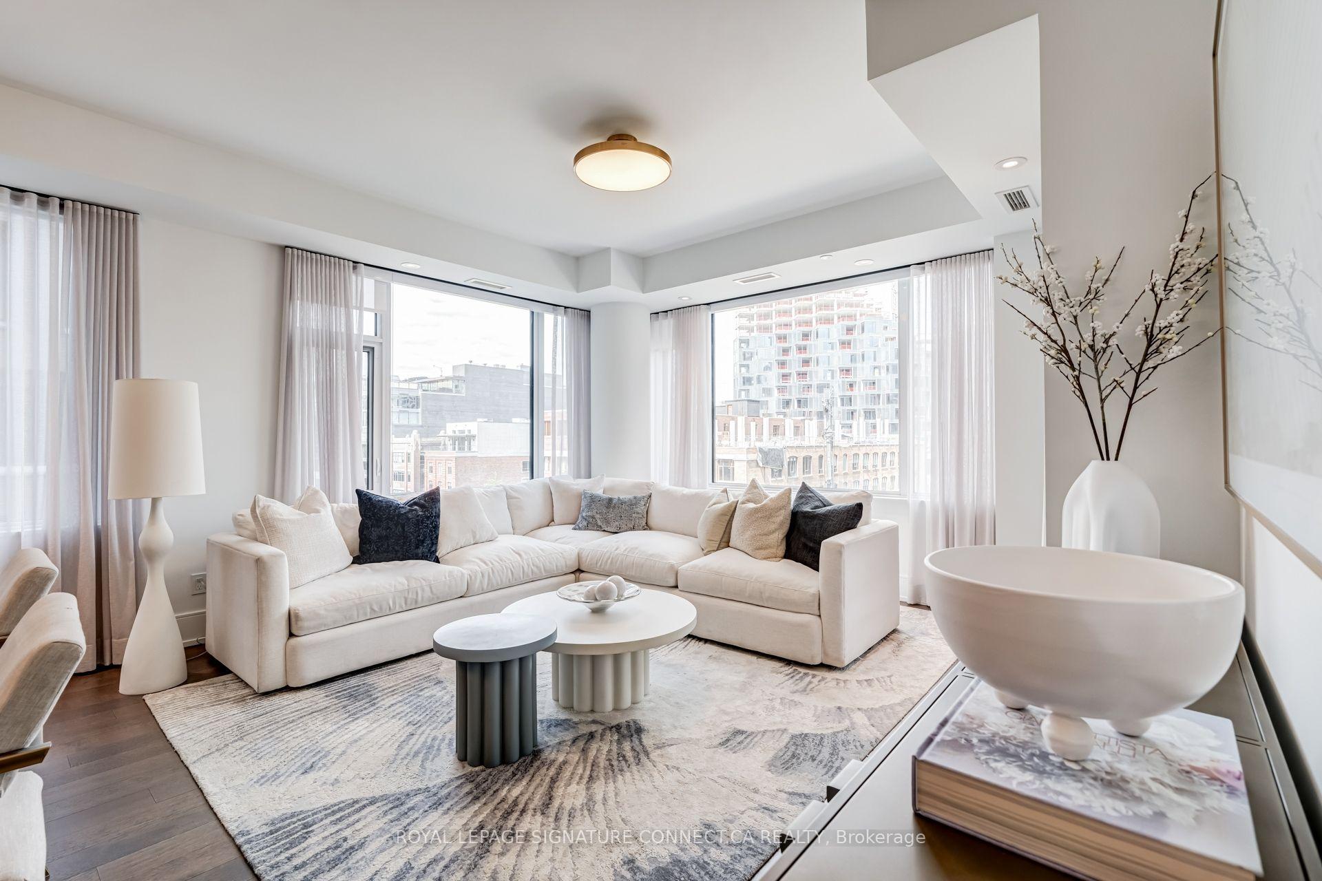 Bright condo living room with a white sectional, round coffee tables, and large windows overlooking nearby buildings.
