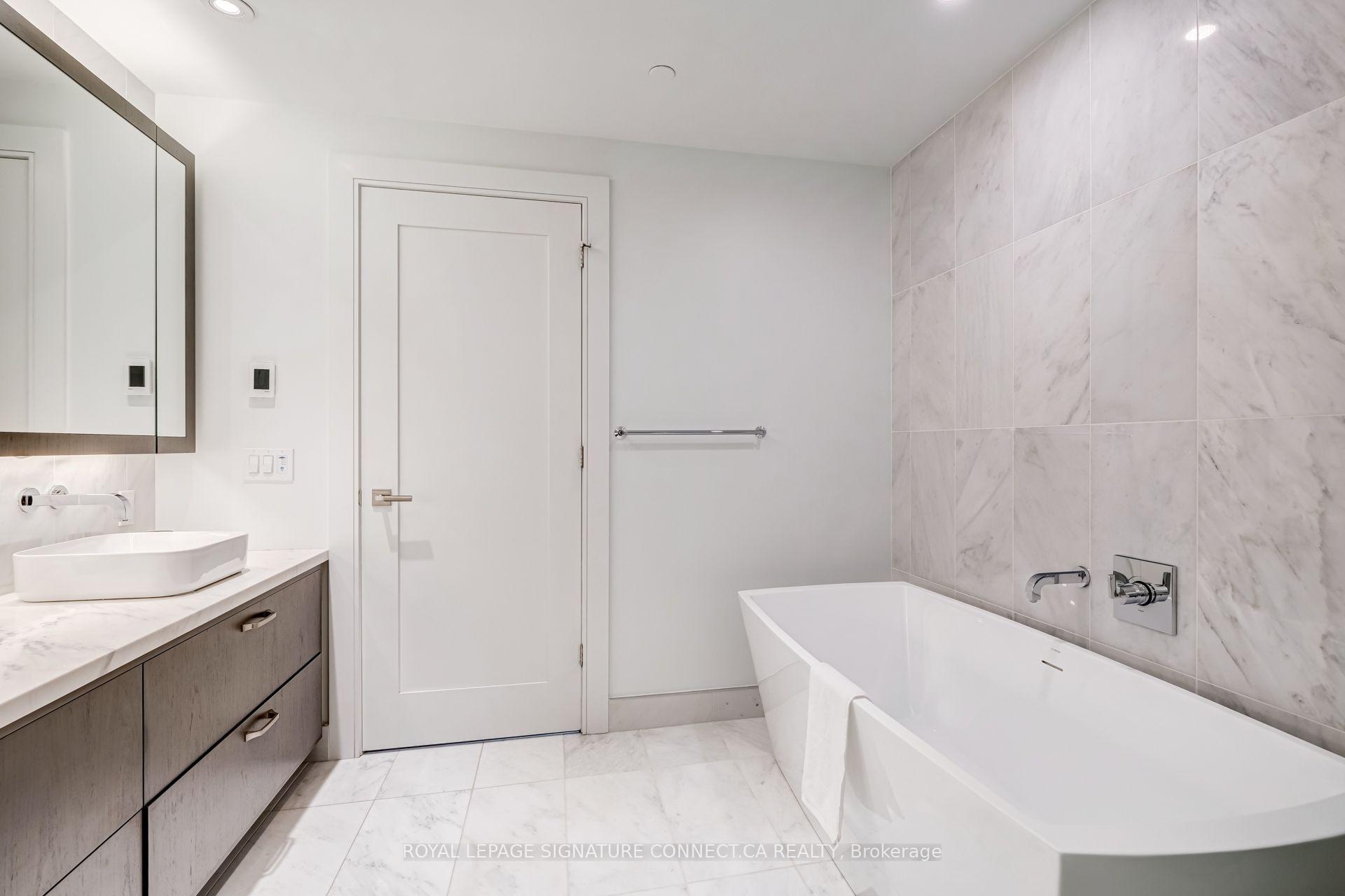 Modern bathroom with freestanding tub, marble-look tile, and a wood-tone vanity.