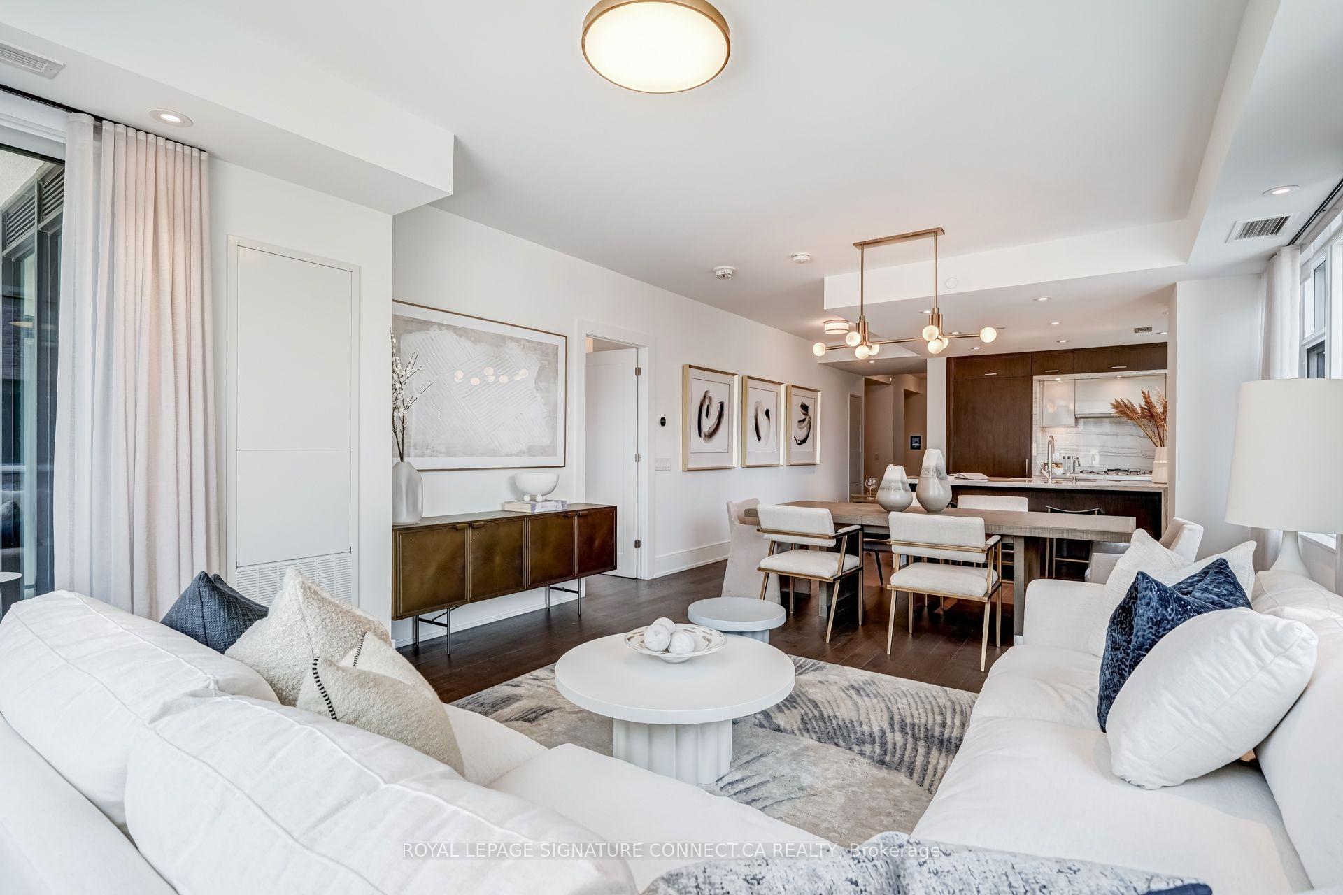 Open-plan condo living and dining area with white sofas, large windows, and a dark wood kitchen.