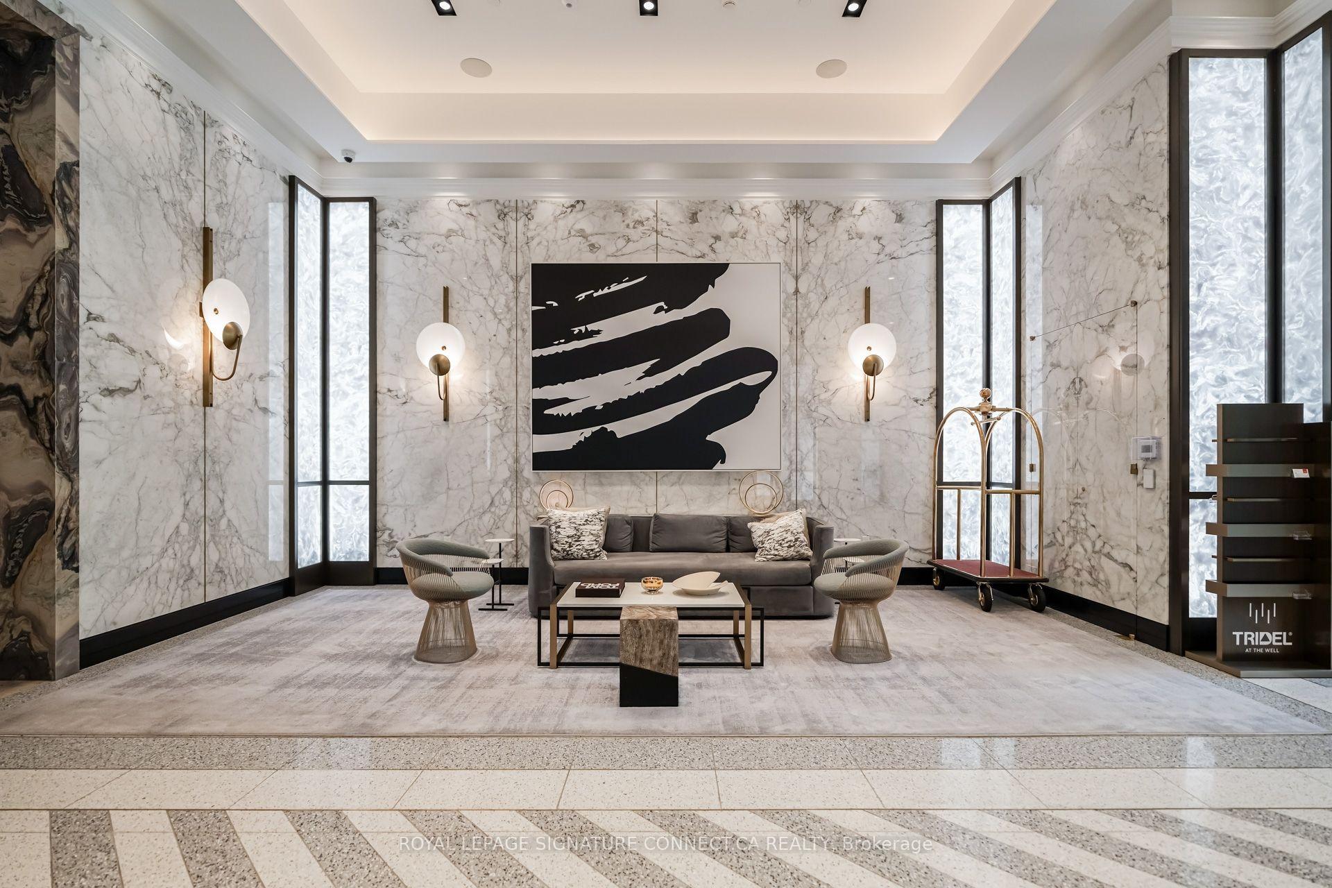 Marble-clad lobby lounge with a gray sofa, sculptural chairs, abstract artwork, and tall windows.