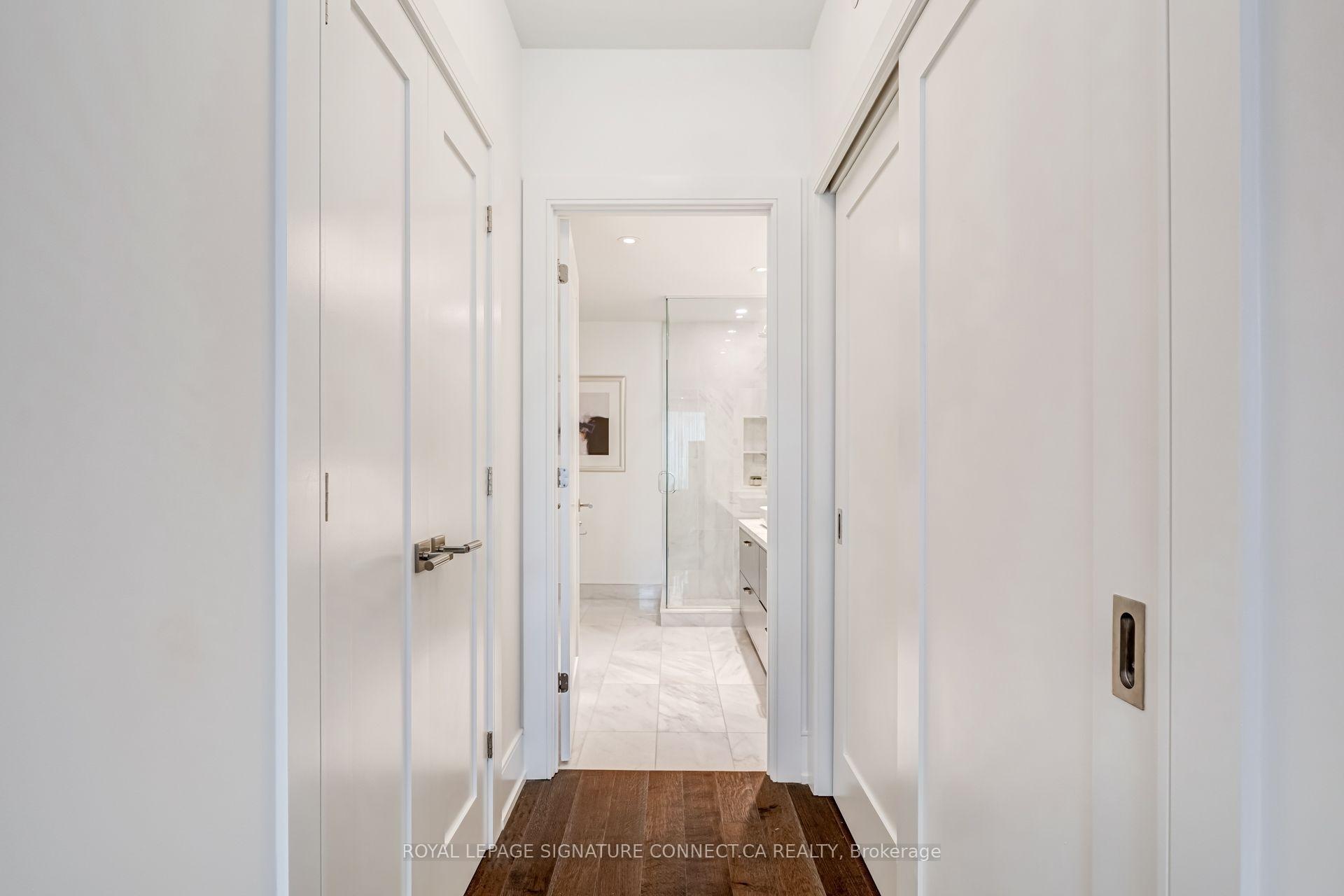 White paneled hallway with dark wood flooring leading to a marble bathroom and glass shower.