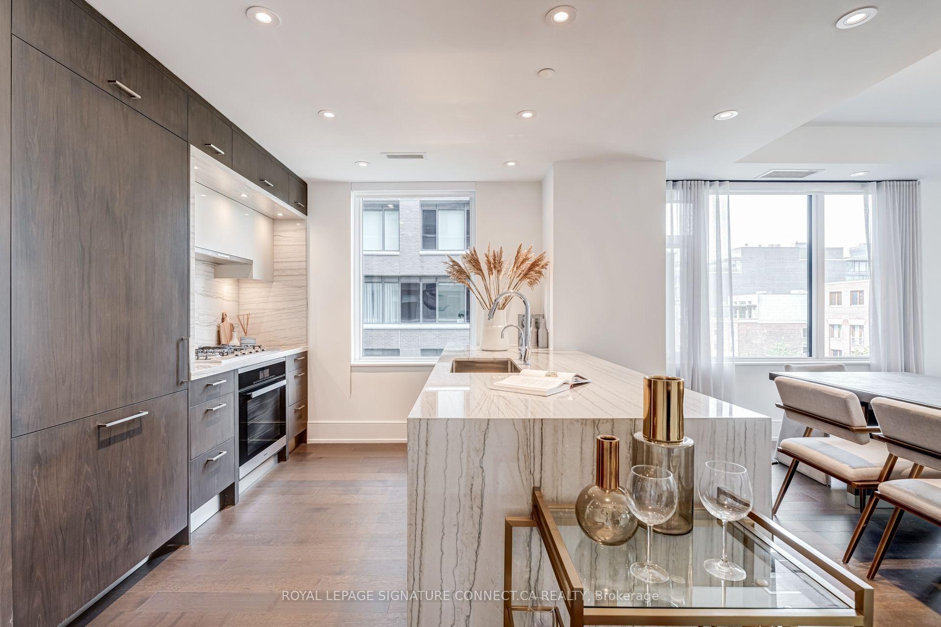 Staged condo kitchen with a veined marble island, dark cabinetry, and a dining area by large windows.
