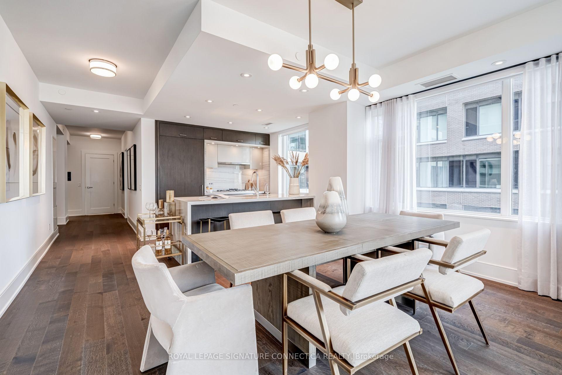 Open-plan condo dining area with a large table, modern kitchen, dark cabinetry, and floor-to-ceiling windows.