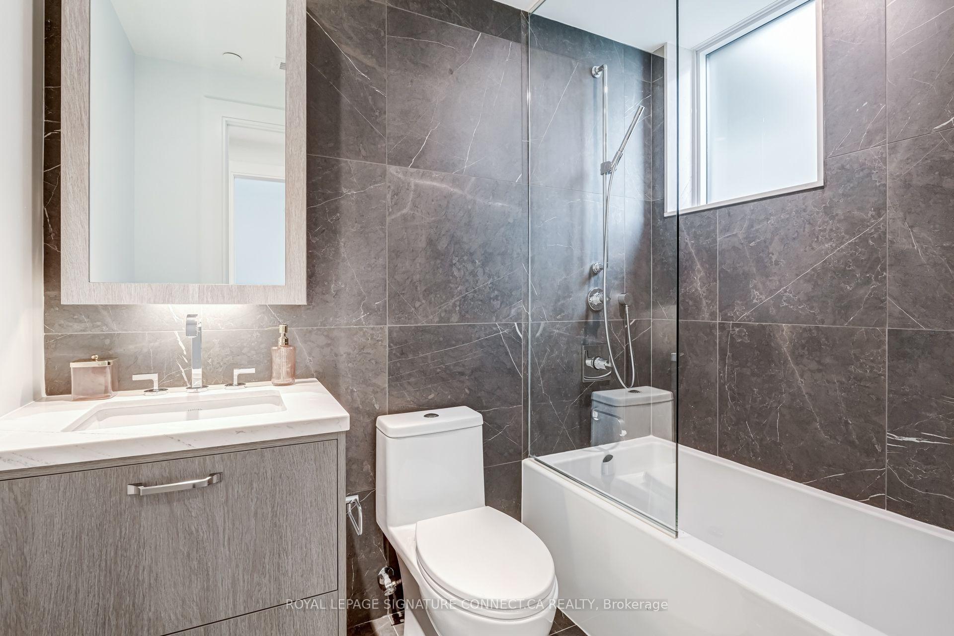 Modern bathroom with dark stone tile, glass-enclosed tub and shower, and gray vanity.