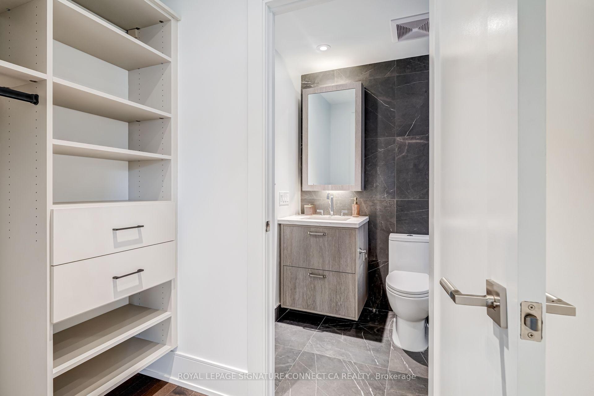 Modern bathroom with a gray vanity and dark marble-look tile, beside built-in white shelving.