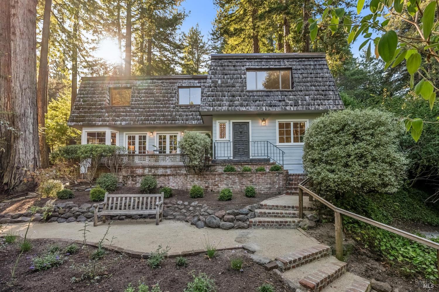 Wooded home with a broad shingle roof, brick terrace, and garden steps.