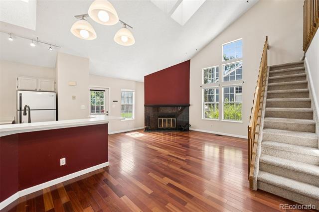 Open-plan living room with hardwood floors, burgundy fireplace wall, tall windows, and carpeted stairs.
