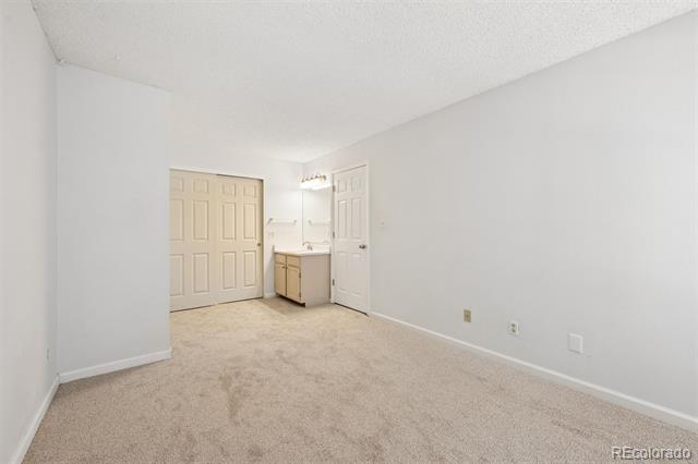 Empty carpeted room with closet doors and a vanity beside the entry door.