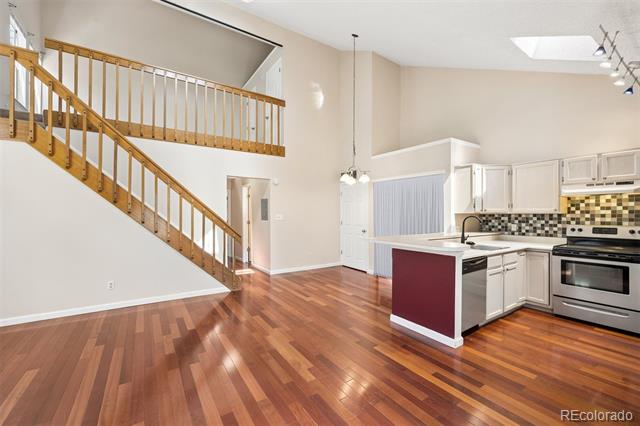 Open-plan kitchen with white cabinetry and island beside a wooden staircase and hardwood floors.