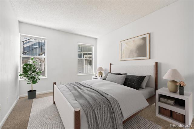 Bedroom with gray bedding, two windows, a potted plant, and framed artwork above the bed.