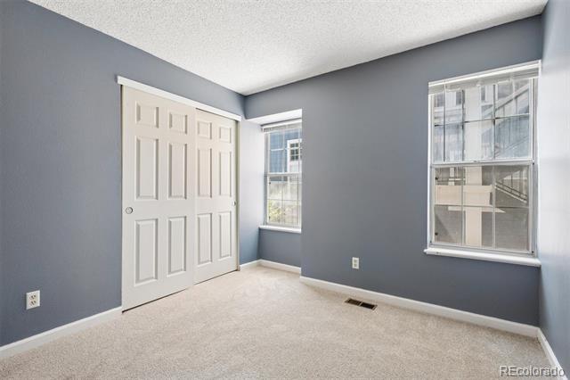 Empty carpeted room with gray walls, white double closet doors, and two windows.