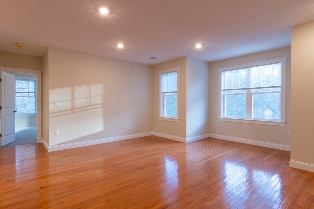 Empty room with polished hardwood floors, two windows, and an open doorway to an adjoining room.