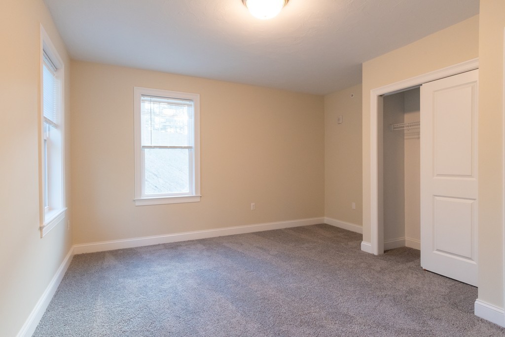 Empty bedroom with gray carpet, two windows, and an open closet.