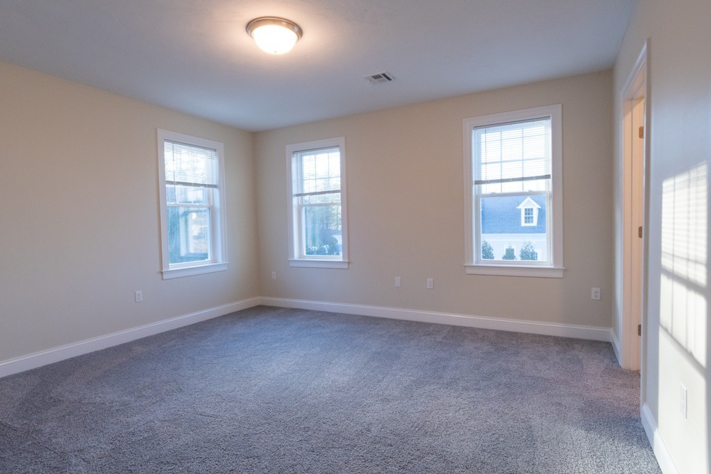 Vacant bedroom with gray carpeting, three windows, and a ceiling light.