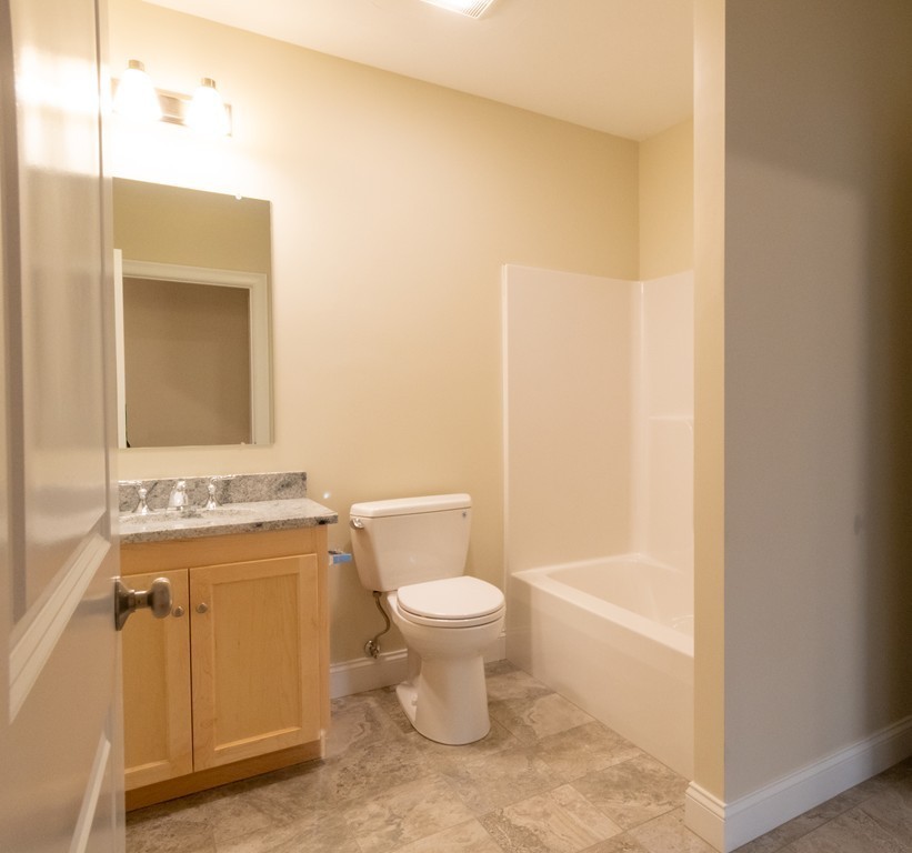 Bathroom with a wood vanity, granite counter, toilet, and white bathtub.