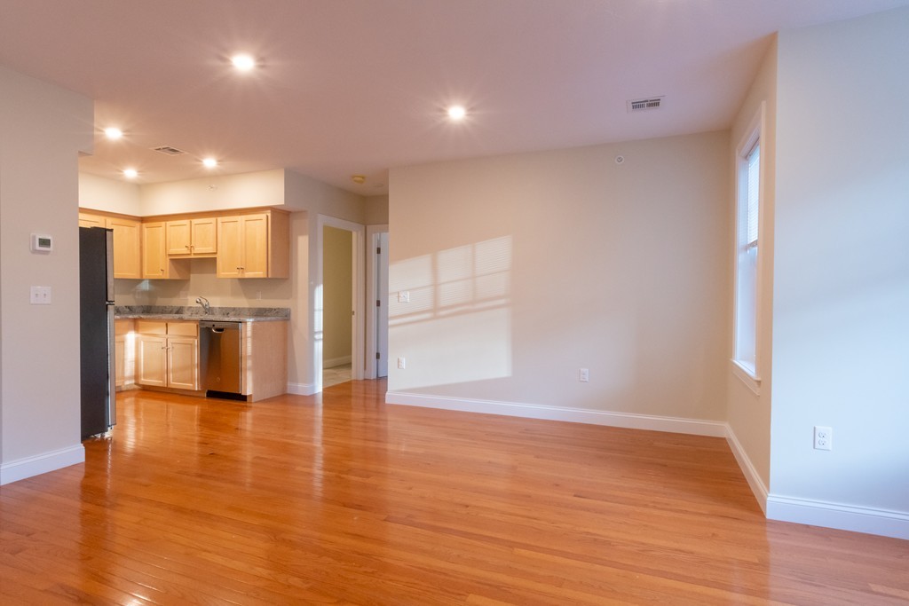 Empty living and dining area with hardwood floors and an open kitchen.