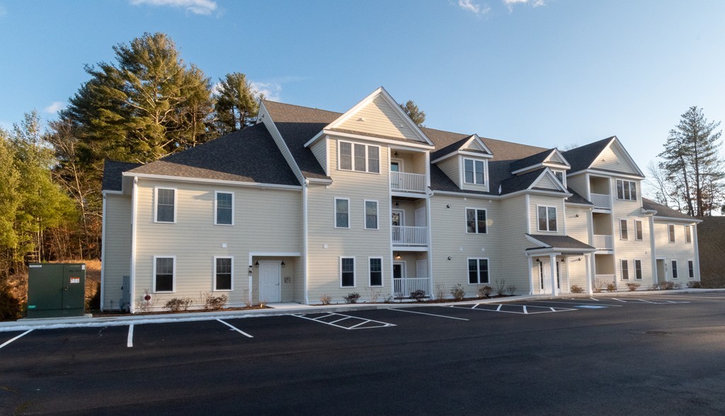 Multi-unit residential building with dark gabled roofs, balconies, and a marked parking lot.
