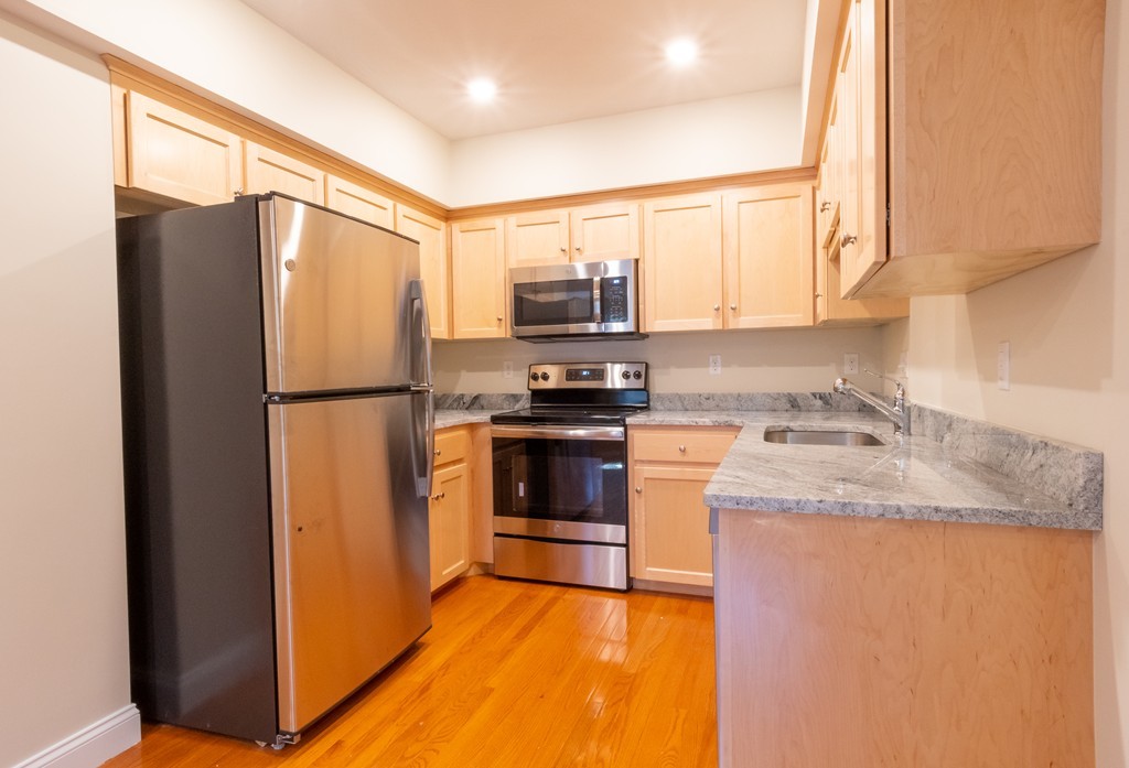 Kitchen with light wood cabinets, granite counters, stainless steel appliances, and hardwood flooring.