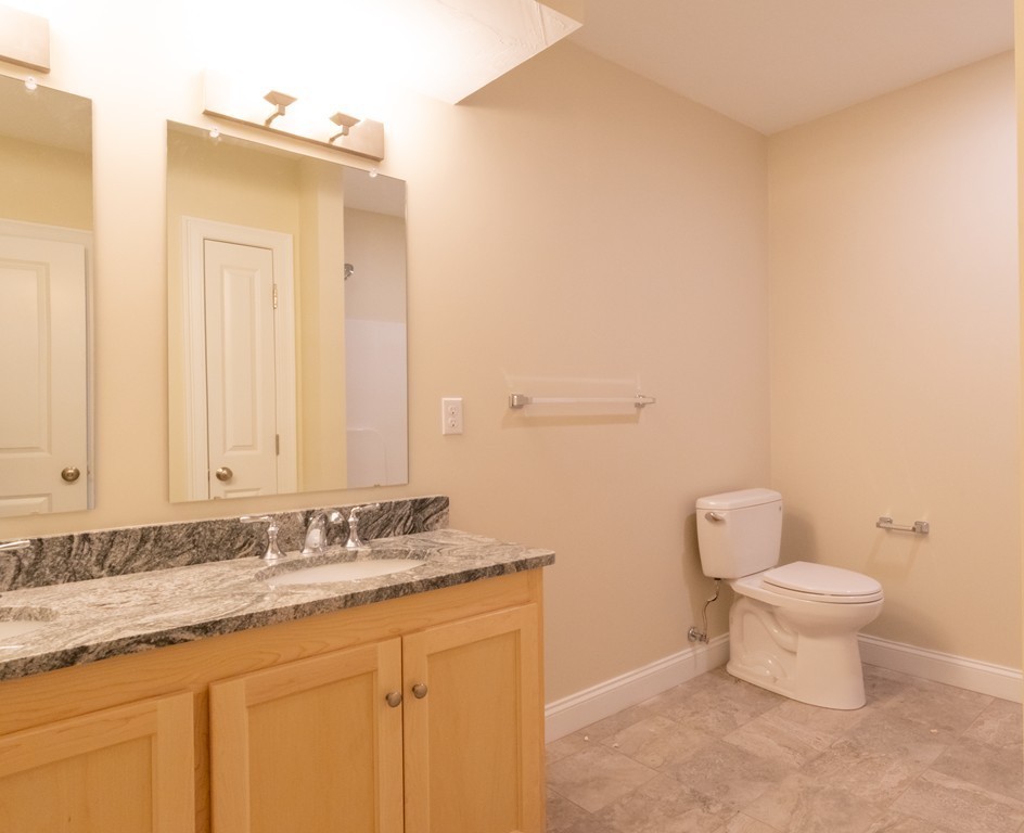 Bathroom with a granite vanity, light wood cabinets, large mirror, and tiled floor.
