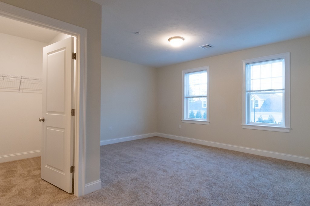 Empty carpeted bedroom with two windows and an open closet.