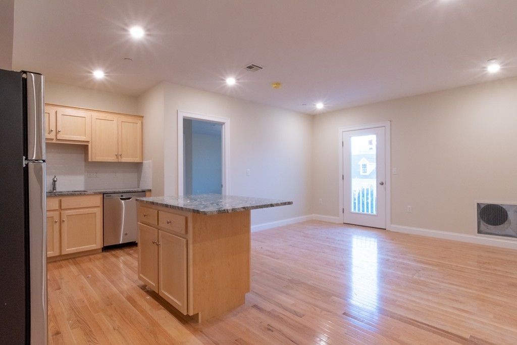 Open kitchen and living area with wood cabinetry, granite island, and hardwood floors.