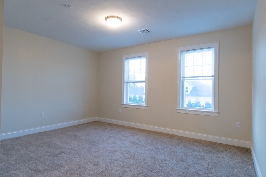 Empty bedroom with gray carpet and two bright windows.