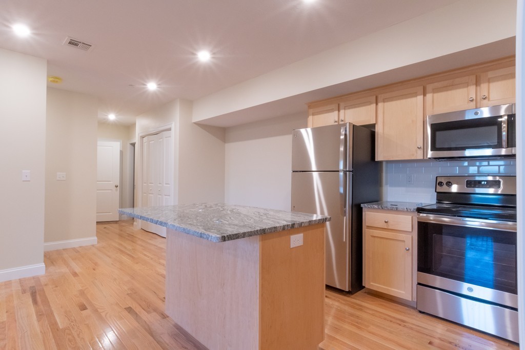Kitchen with a granite-topped island, light wood cabinets, and stainless steel appliances.