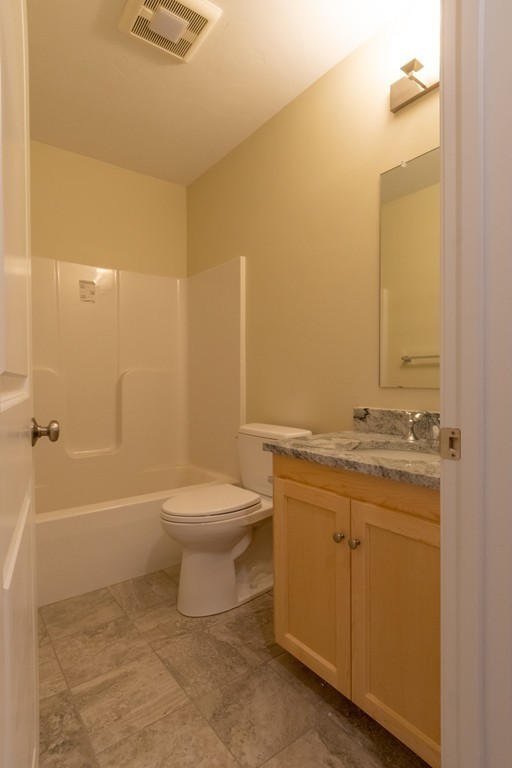 Bathroom with a bathtub and shower, toilet, and wood vanity with a stone countertop.