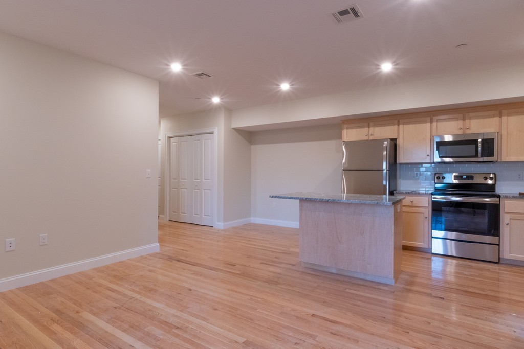 Open kitchen with a stone island, stainless steel appliances, and hardwood floors.
