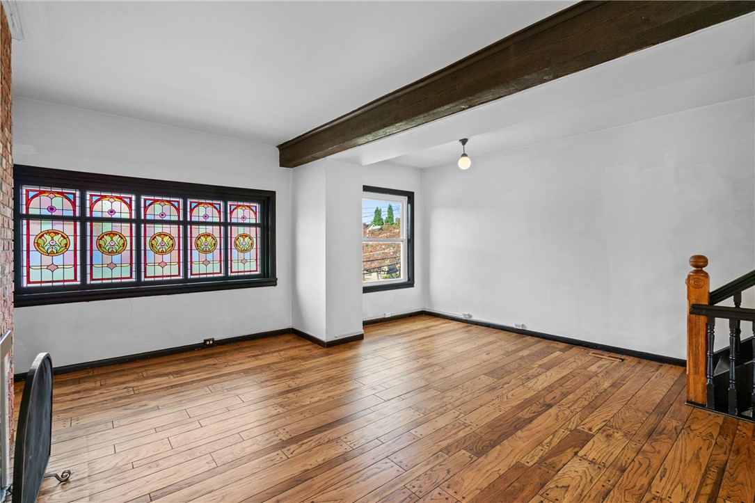Empty room with hardwood floors, stained-glass windows, an exposed beam, and a staircase railing.