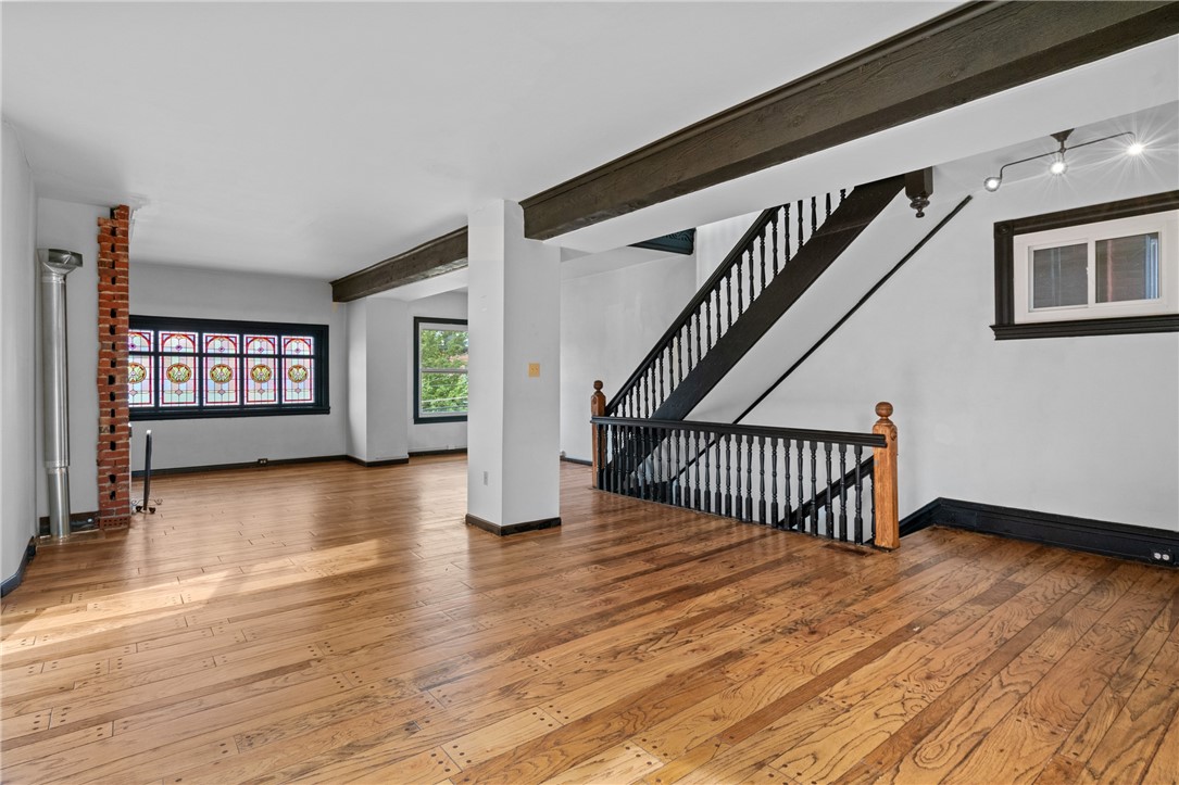 Unfurnished room with hardwood floors, exposed beams, a black staircase, and stained-glass windows.