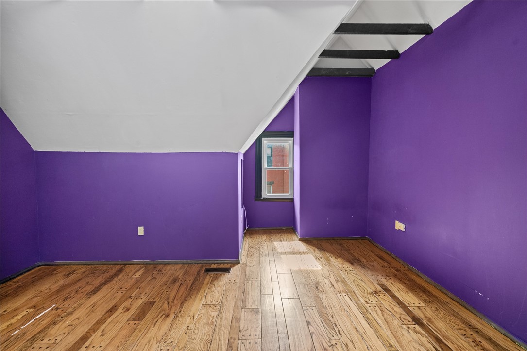 Empty room with purple walls, a sloped ceiling, overhead stair treads, and hardwood floors.