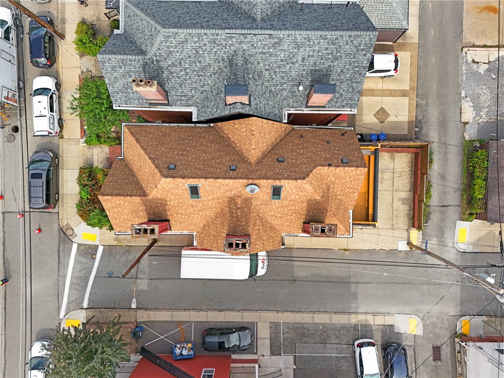 Aerial view of a brick building with brown and gray shingle roofs beside a city street.