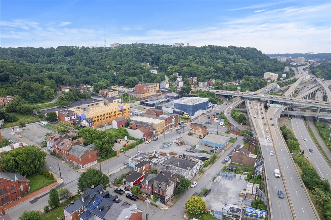 Aerial view of an urban neighborhood beside a highway interchange, with a wooded hillside beyond.