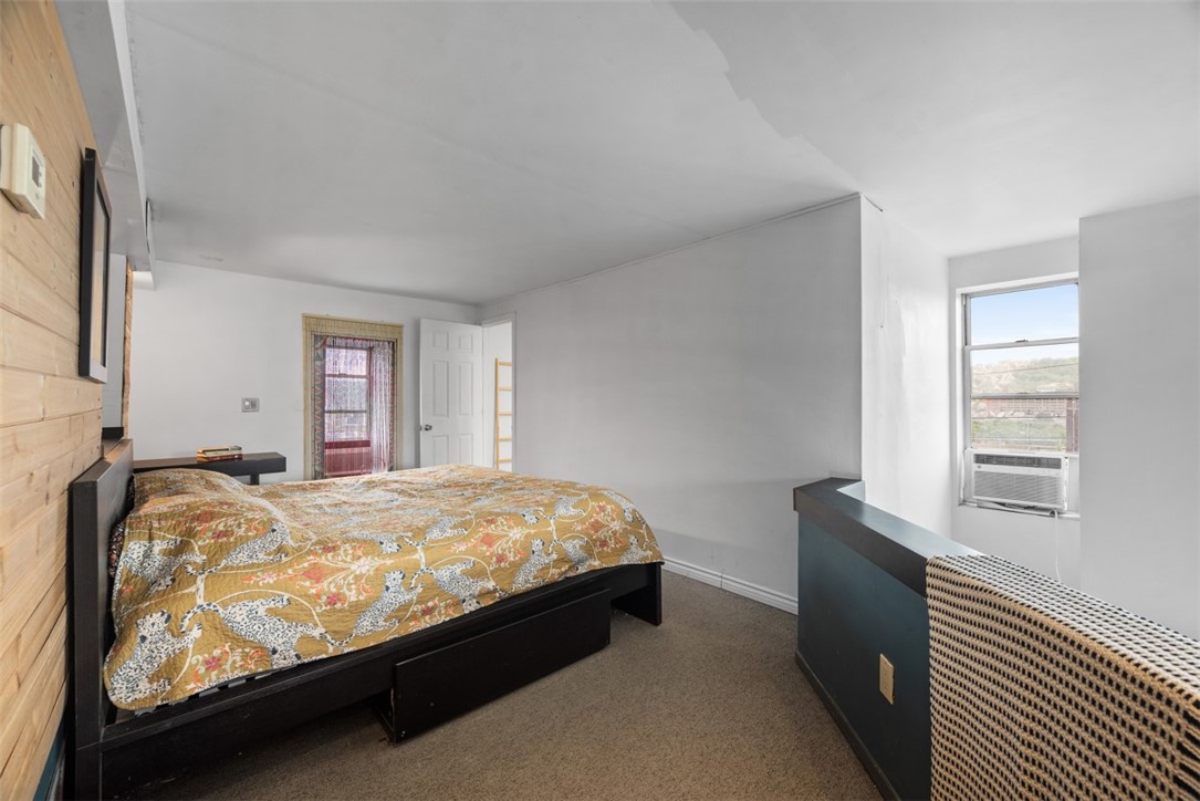 Bedroom with a colorful patterned bedspread, wood-paneled wall, and window air conditioner.