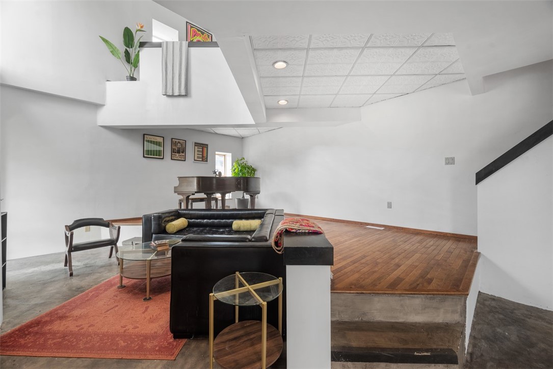 Loft living room with a black leather sectional, grand piano, and raised hardwood-floor area.