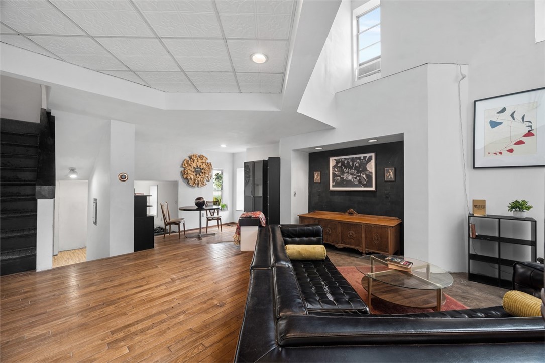 Open-plan living room with hardwood floors, a black leather sectional, and high ceilings.
