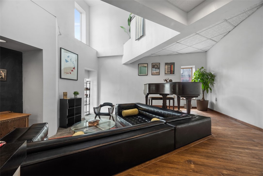 Loft living room with a grand piano, dark leather sofas, and wide-plank wood floors.