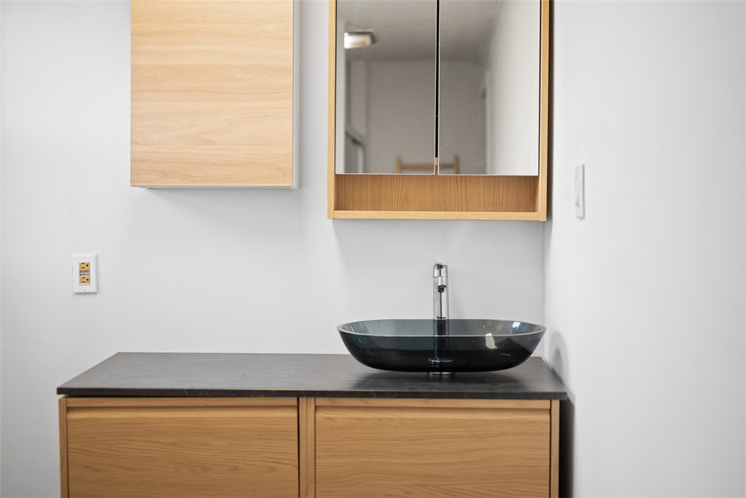 Bathroom vanity with a black vessel sink, dark countertop, and light wood cabinetry.