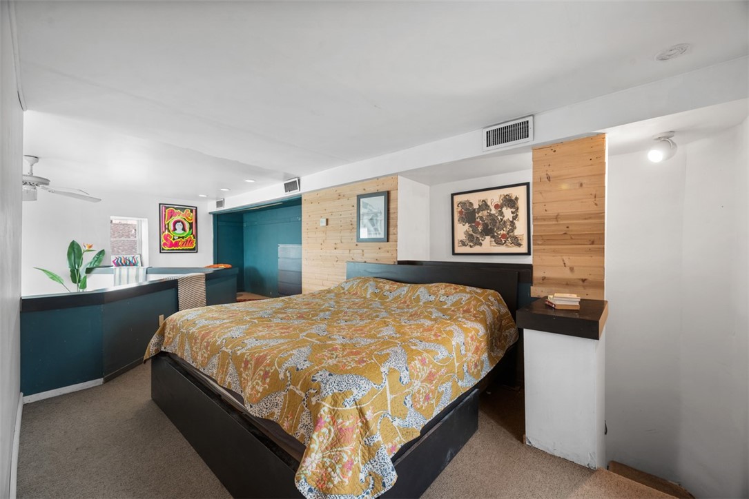 Bedroom with a patterned quilted bed, teal cabinetry, and light wood wall panels.