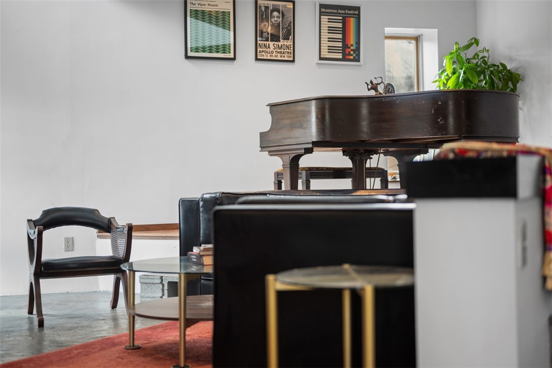Living room with a dark grand piano, black leather seating, and framed music posters.