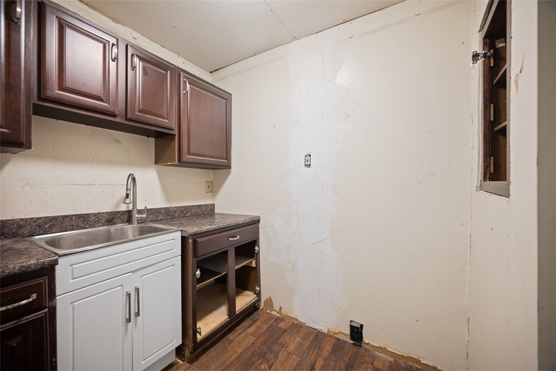 Kitchen with dark wood upper cabinets, a sink, and unfinished walls and flooring.